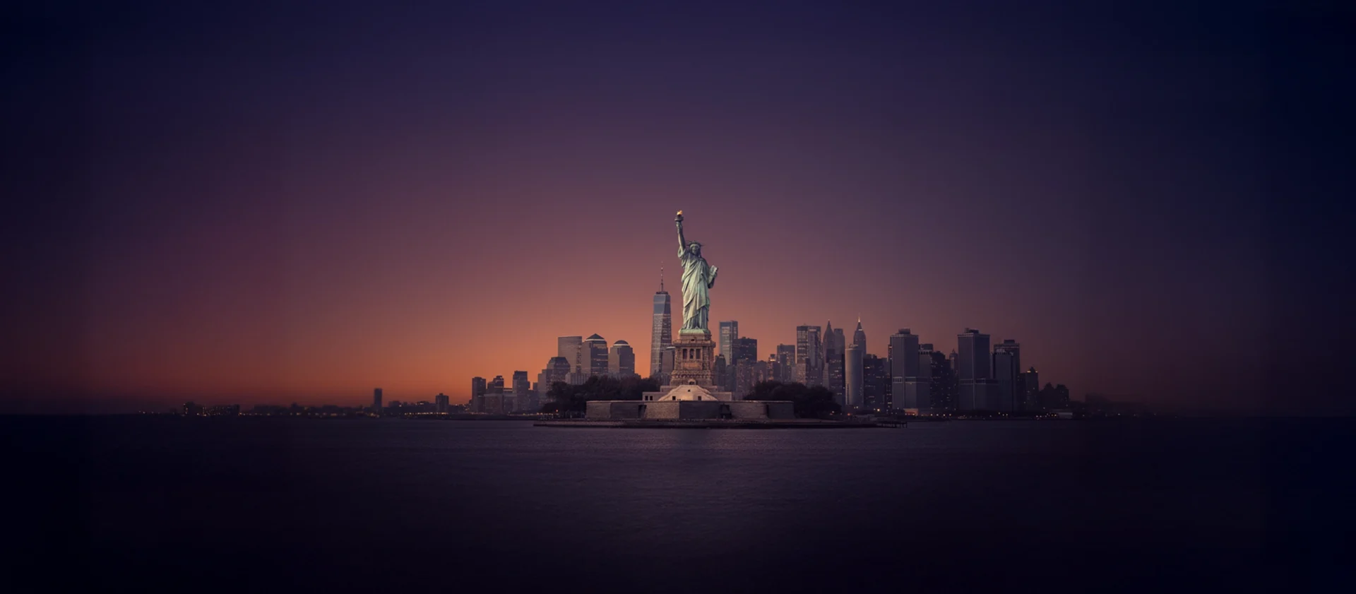 statue of liberty at sunset with new york skyline in background